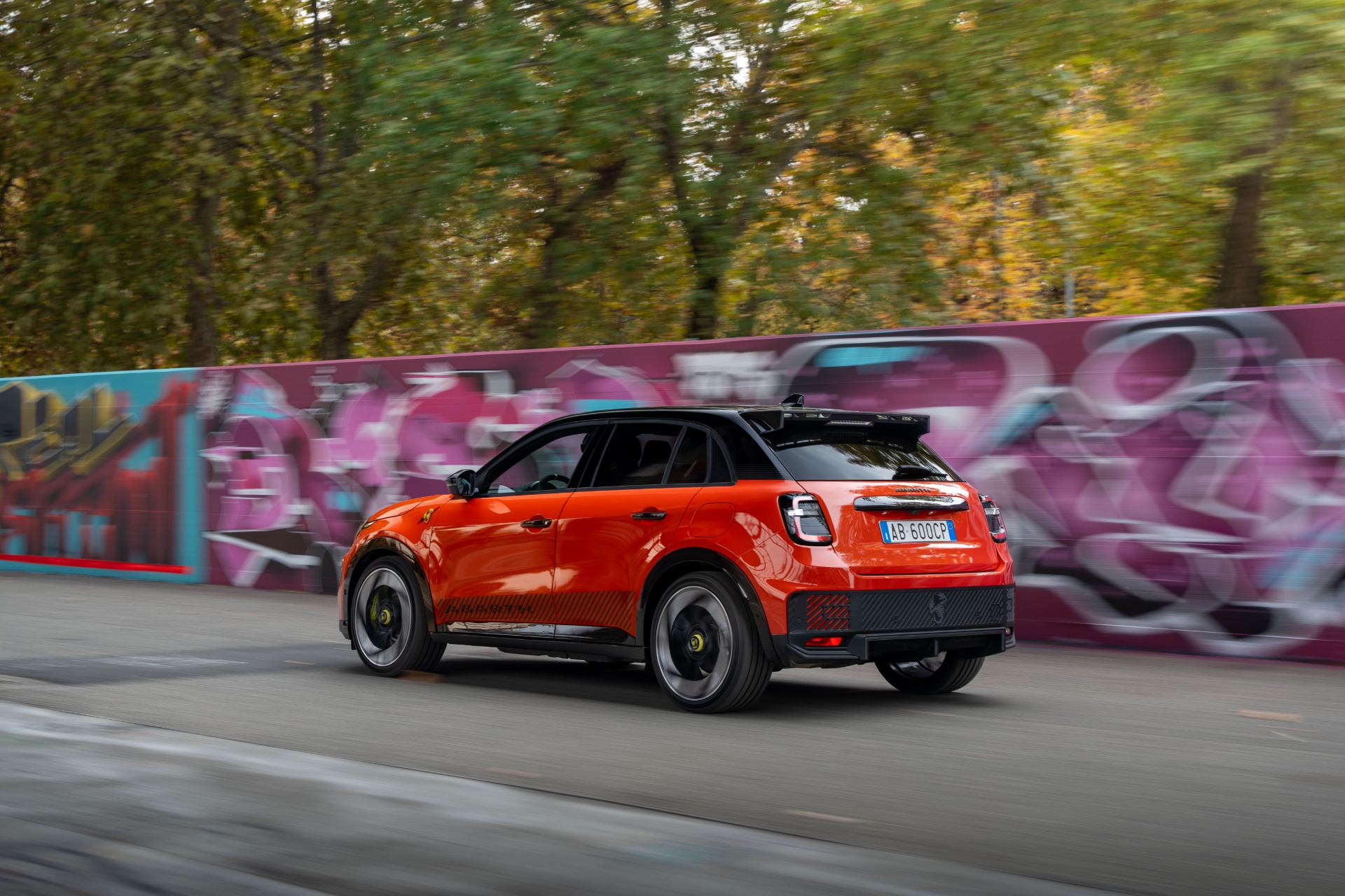 2025 abarth 600e driving rear three quarter graffiti wall orange