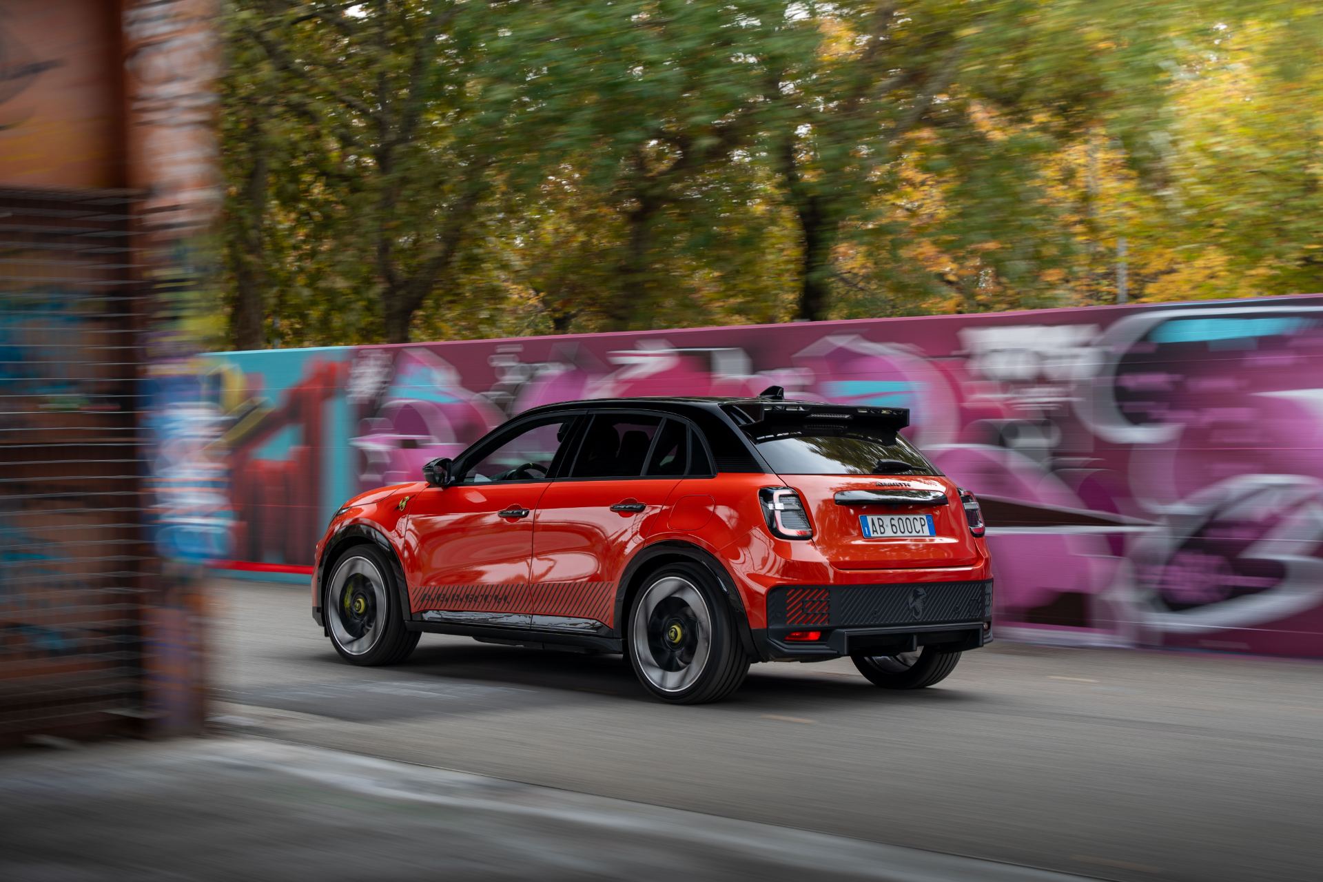 2025 abarth 600e driving rear three quarter orange