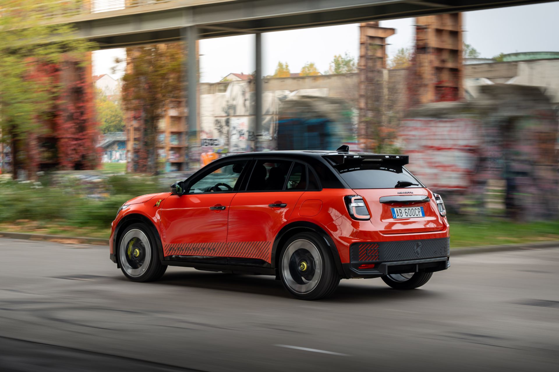 2025 abarth 600e driving rear three quarter industrial orange