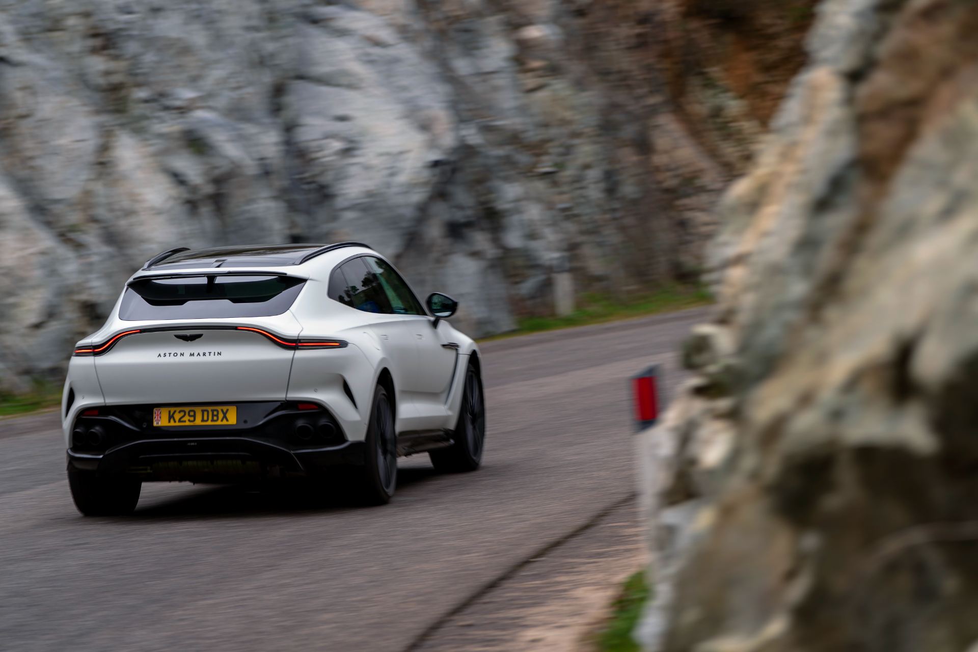 2026 aston martin dbx707 driving rear three quarter rock wall white