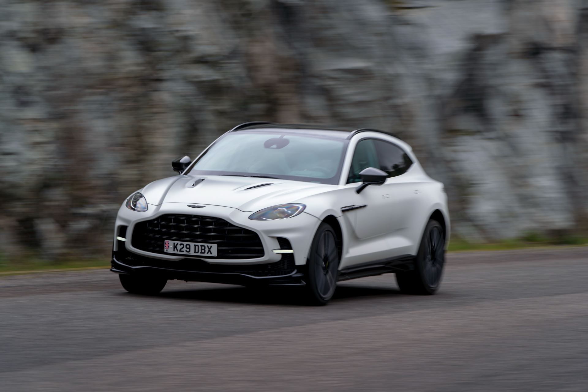 2026 aston martin dbx707 driving front three quarter rock wall white