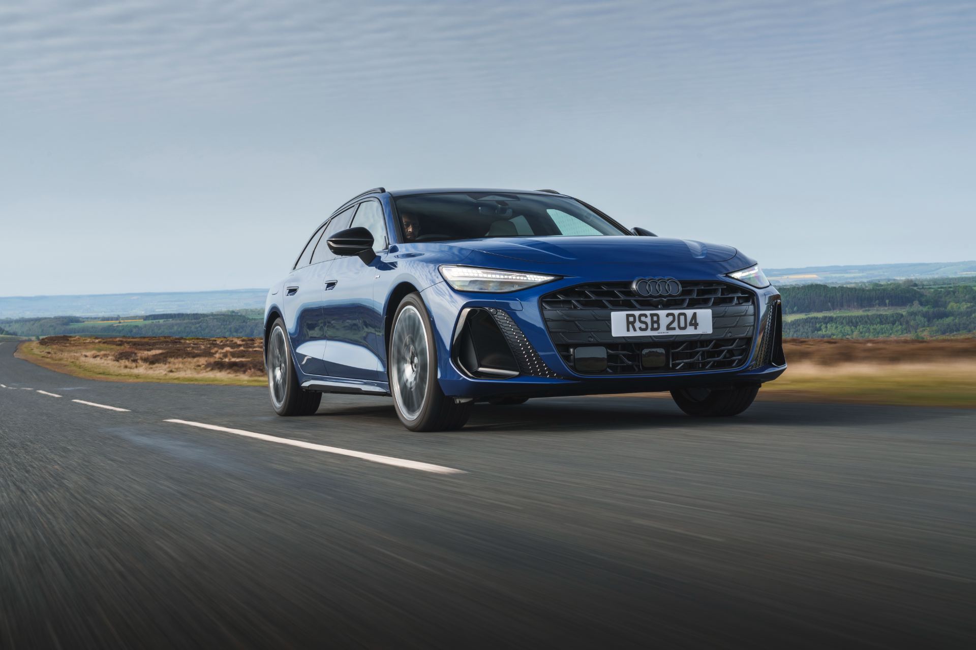 2026 audi a6 avant driving front three quarter moorland road blue
