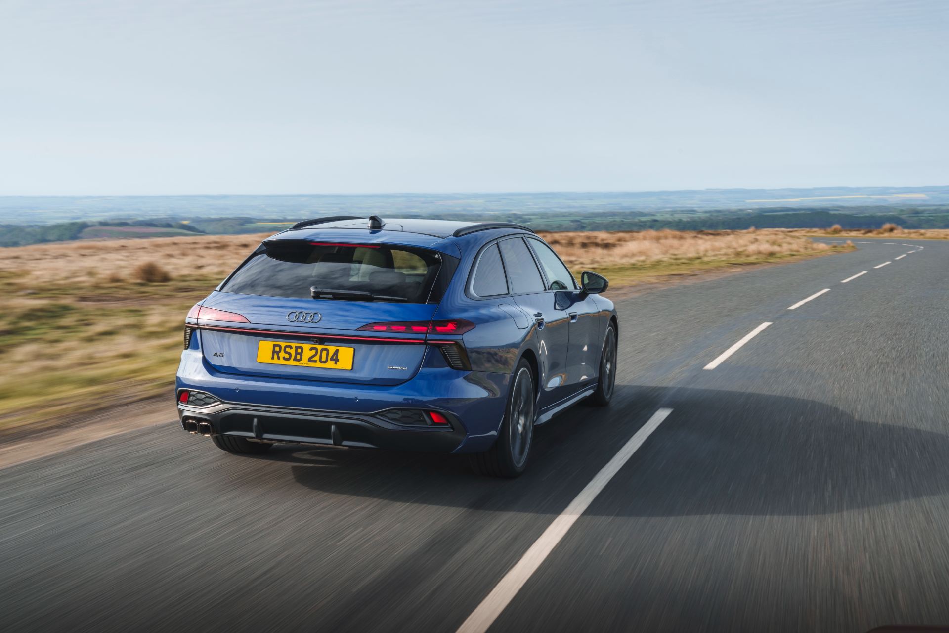 2026 audi a6 avant driving rear three quarter moorland road blue