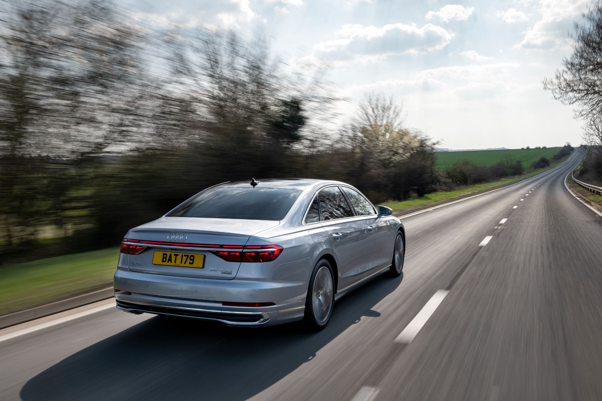 2025 audi a8 60 tfsi e driving rear three quarter road silver