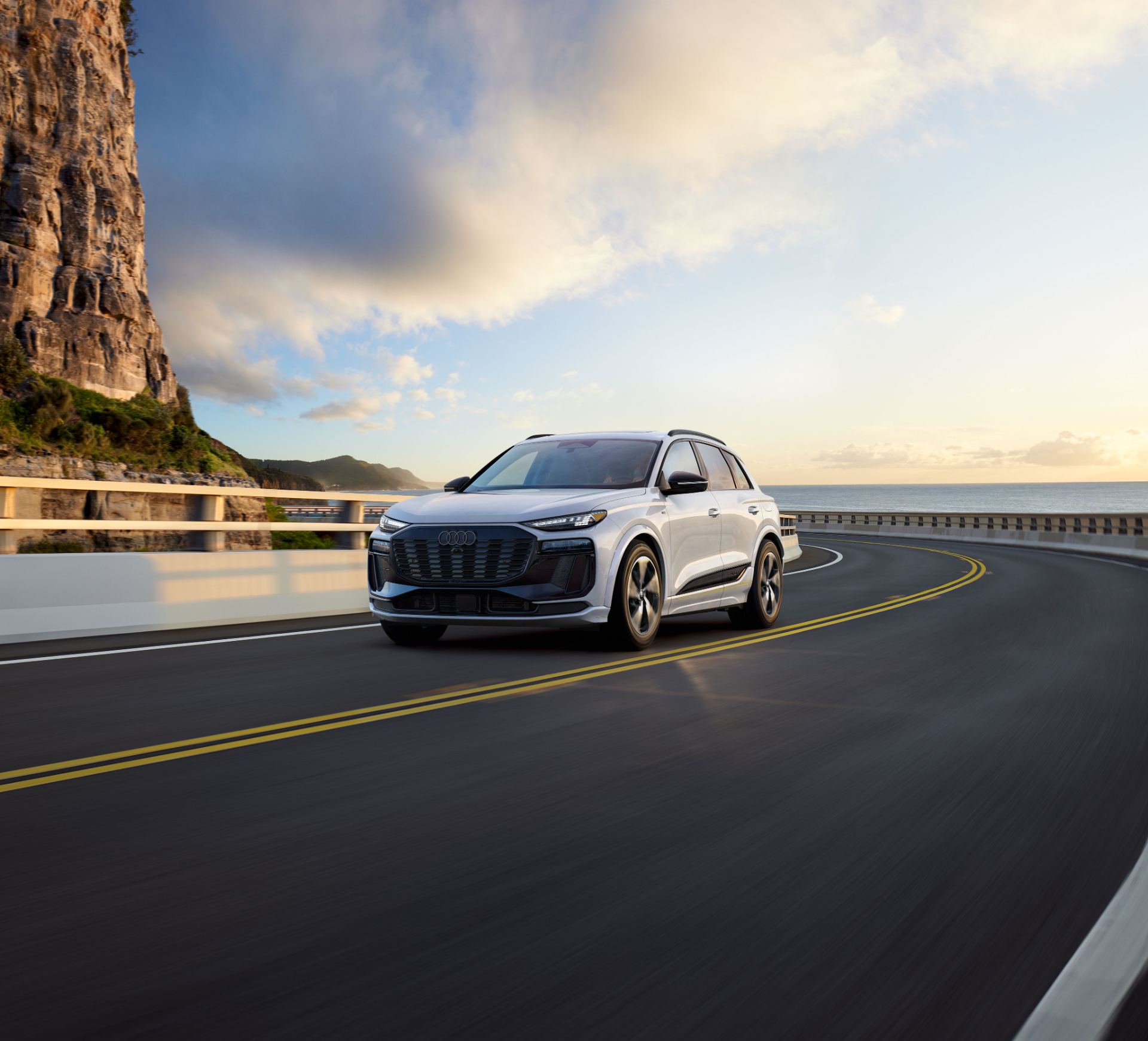 2027 audi q6 e tron driving front three quarter coastal road white