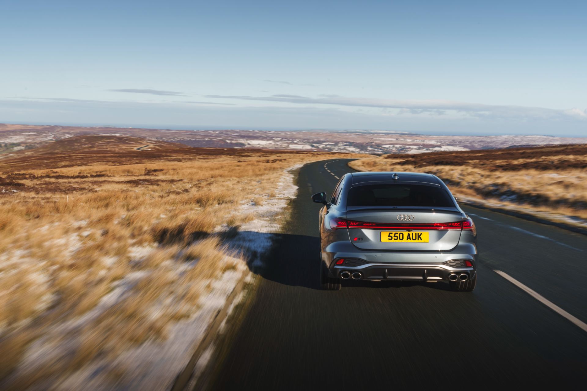 2026 audi s5 saloon driving rear high angle moorland road grey