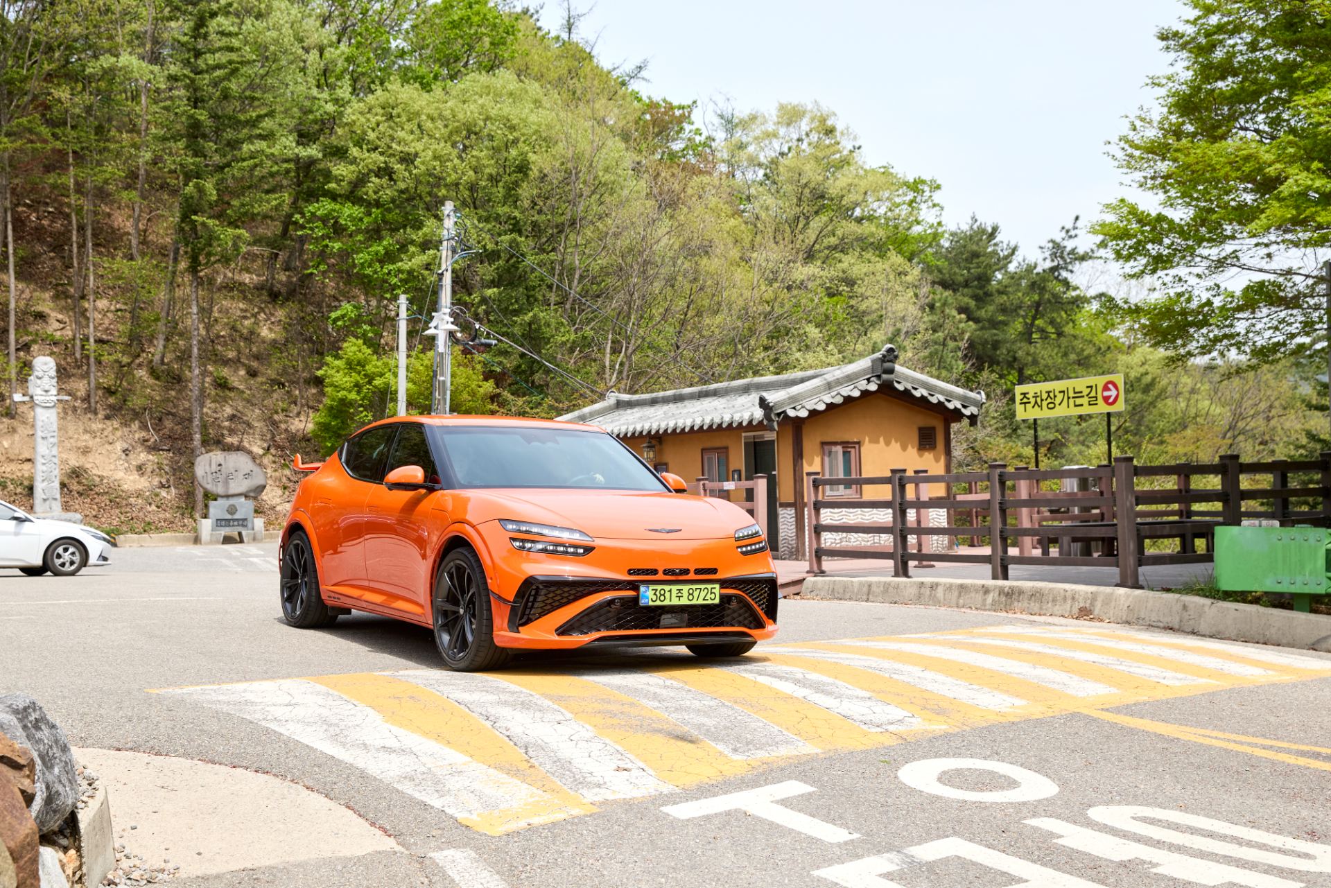 Front three-quarter exterior of the 2027 Genesis GV60 Magma in signature Magma Orange, showing the front canards and wider lower stance, official press photo