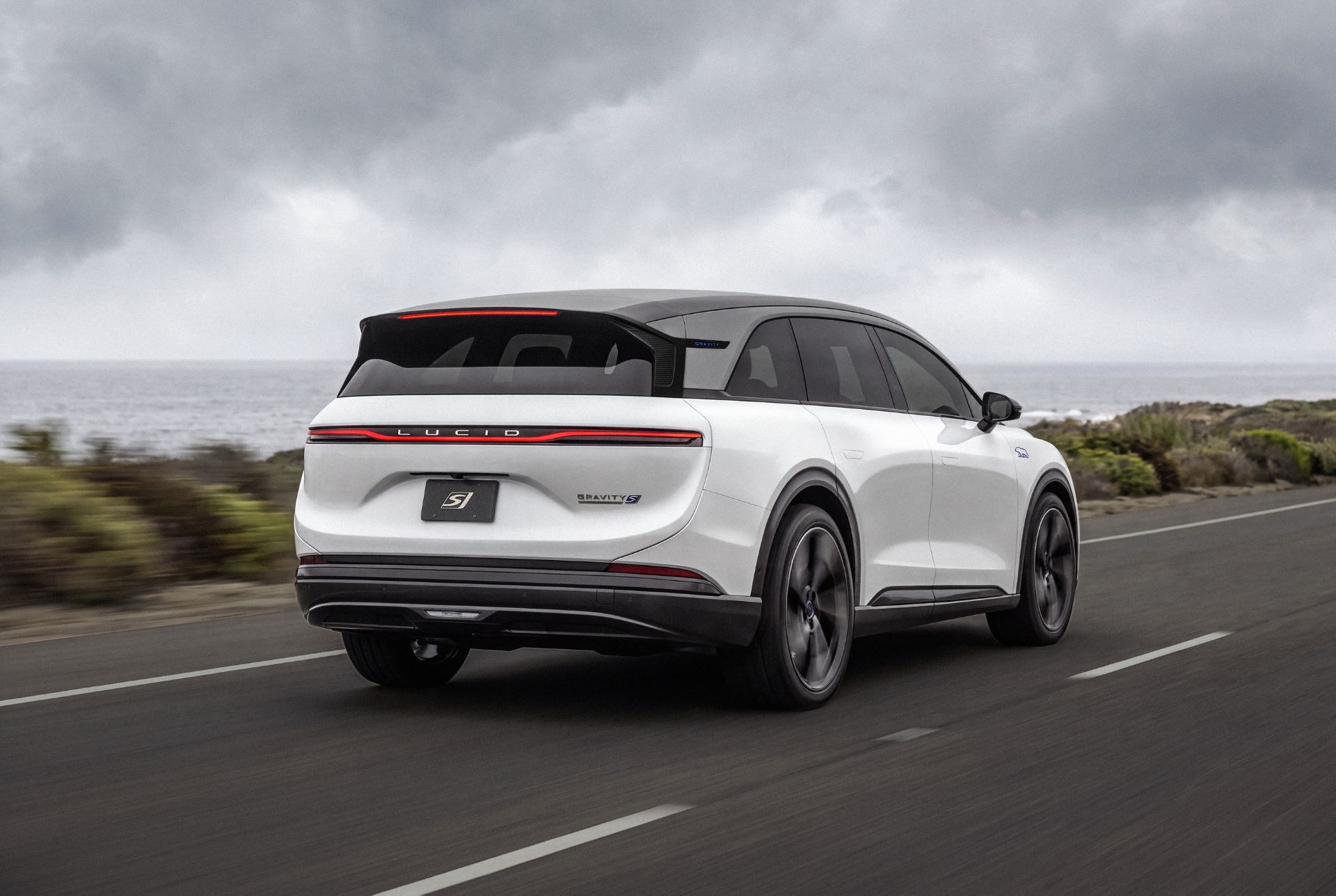 Rear three-quarter in white on a coastal highway showing the full-width tail light bar