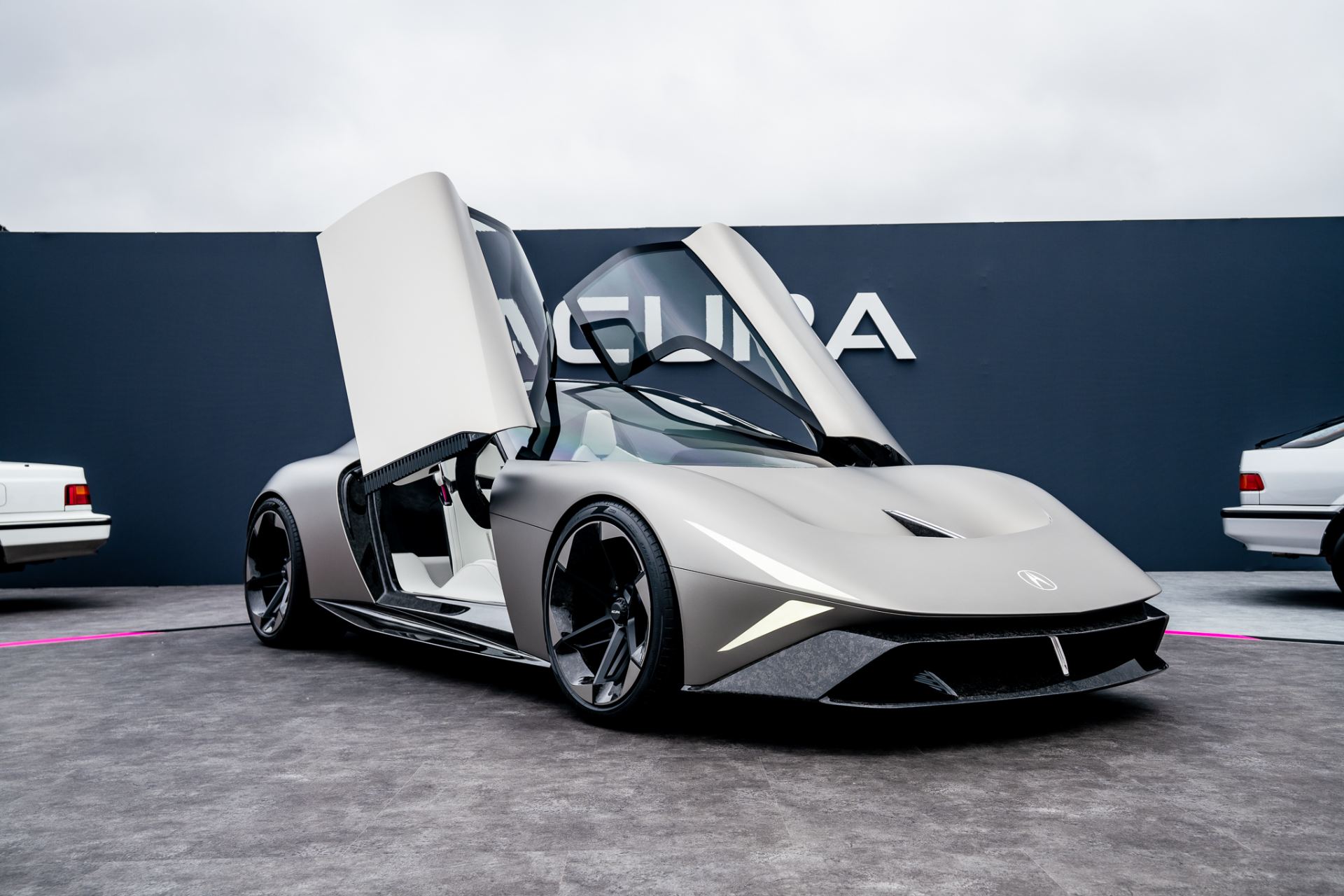 Front three-quarter of the Acura NEXERA Vision concept in Matte Titanium at Monterey Car Week, official press photo showing the butterfly doors and phantom lighting signature